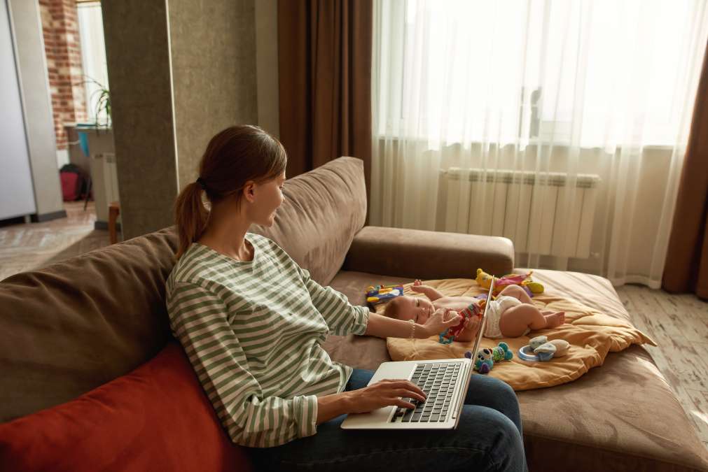 Beautiful mother works with laptop and sits with small child at home- New Role As Parent