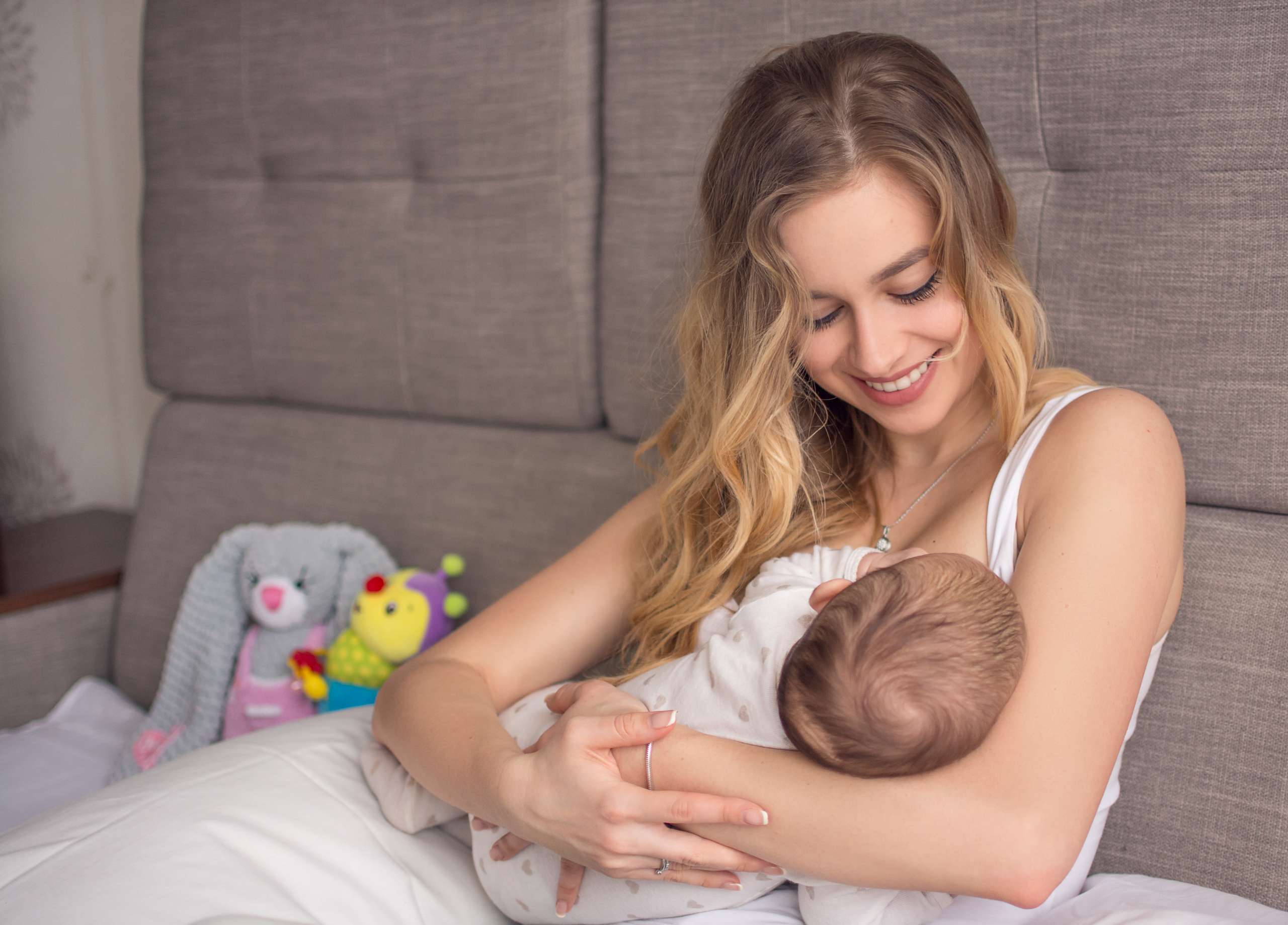 Breastfeeding baby. Pretty mother holding her newborn child. Mom smile and nursing infant. Beautiful woman and new born love at home. Blond mother breast feeding baby- Postpartum Depression And Perfectionism