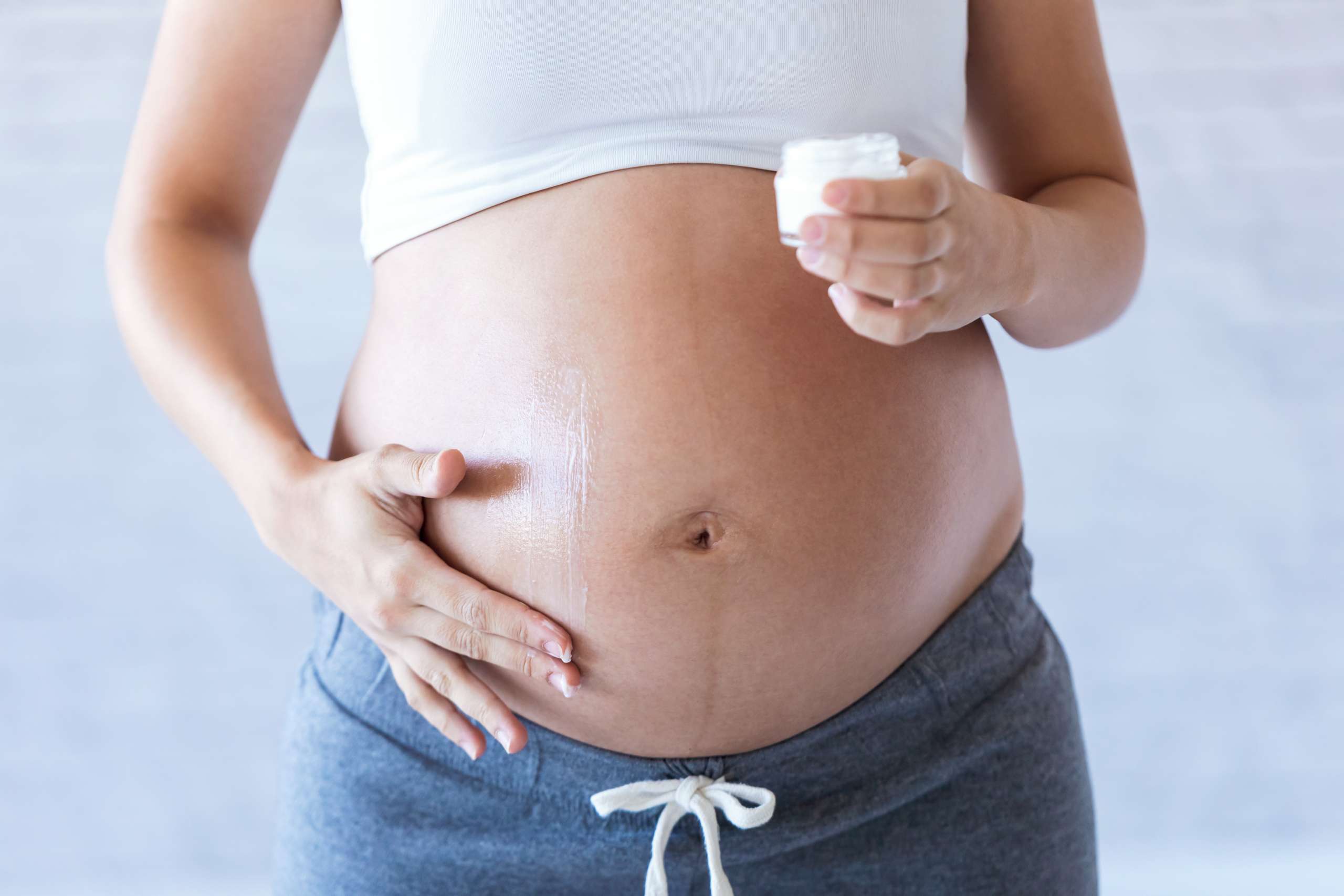 Pregnant woman applying cream lotion on pregnant belly to prevent stretch mark.