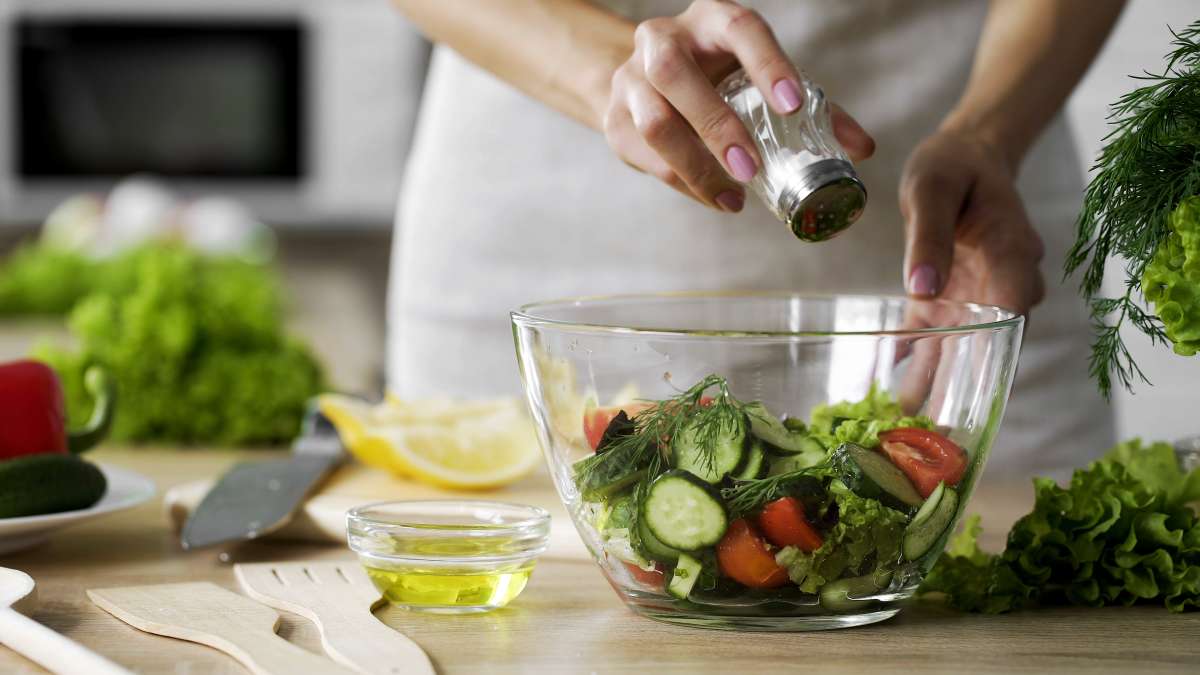 Woman adding salt in vegetable salad glass bowl, health care, excessive salting- Diet During Pregnancy