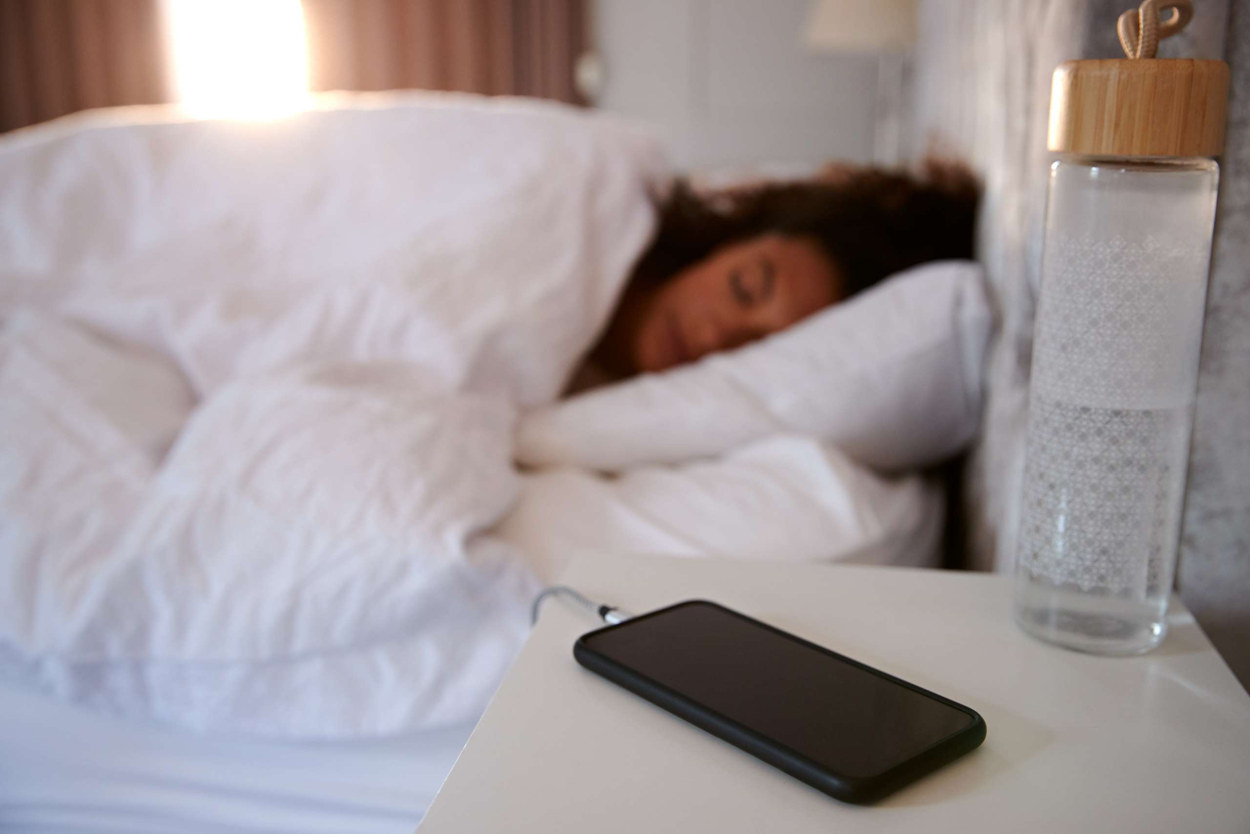 Woman Asleep In Bed With Mobile Phone On Bedside Table