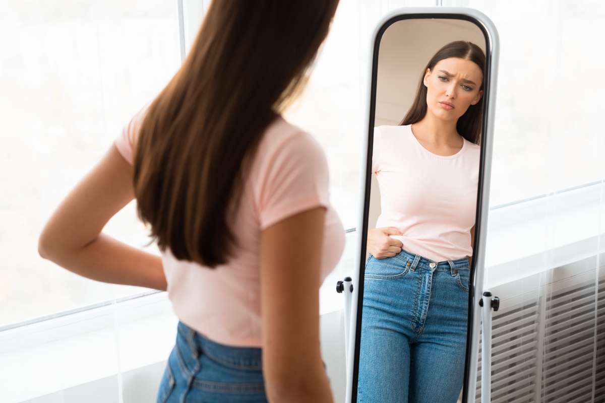 Sad Woman Measuring Waist After Weight Gain Standing At Home