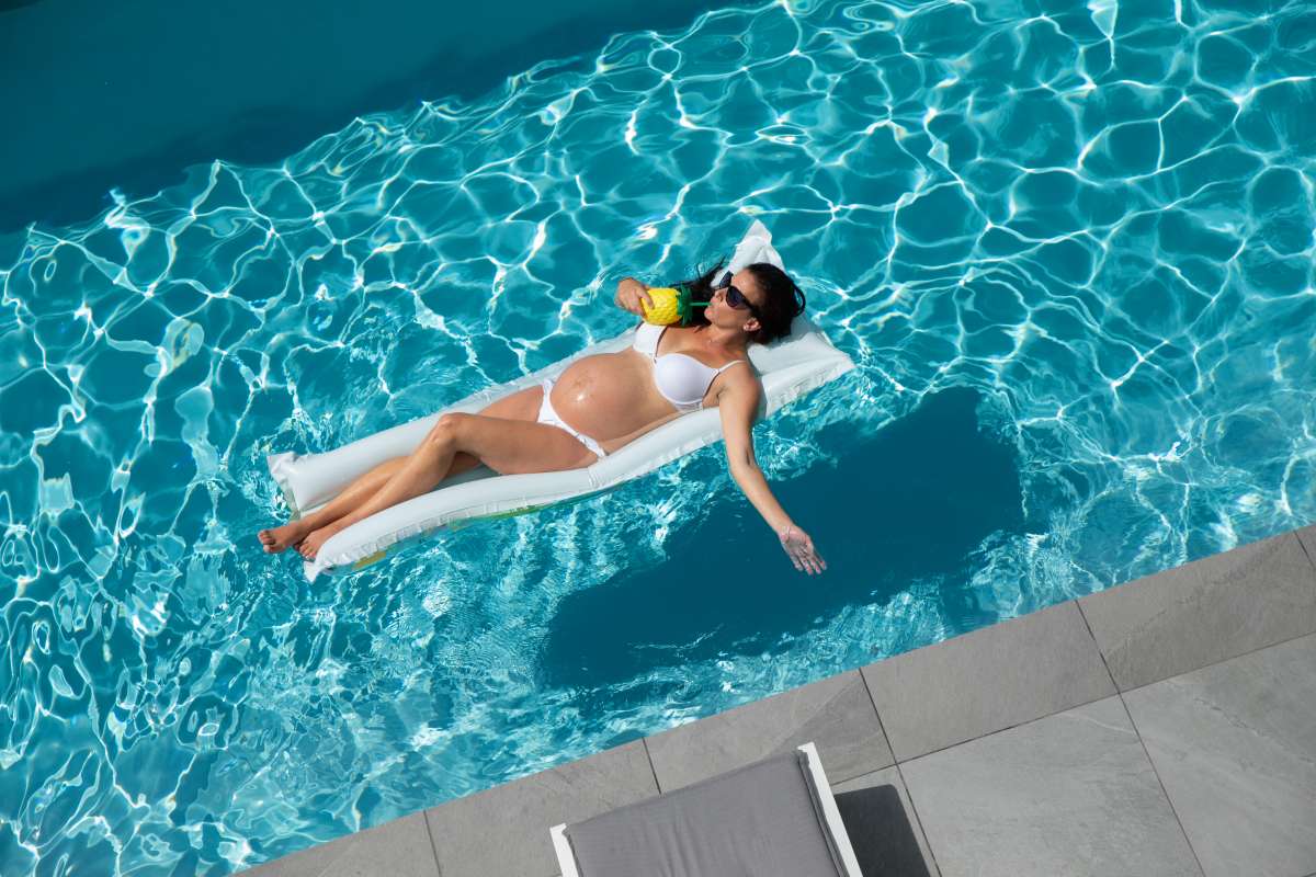 Pregnant woman sunbathing on inflatable mat in a swimming pool