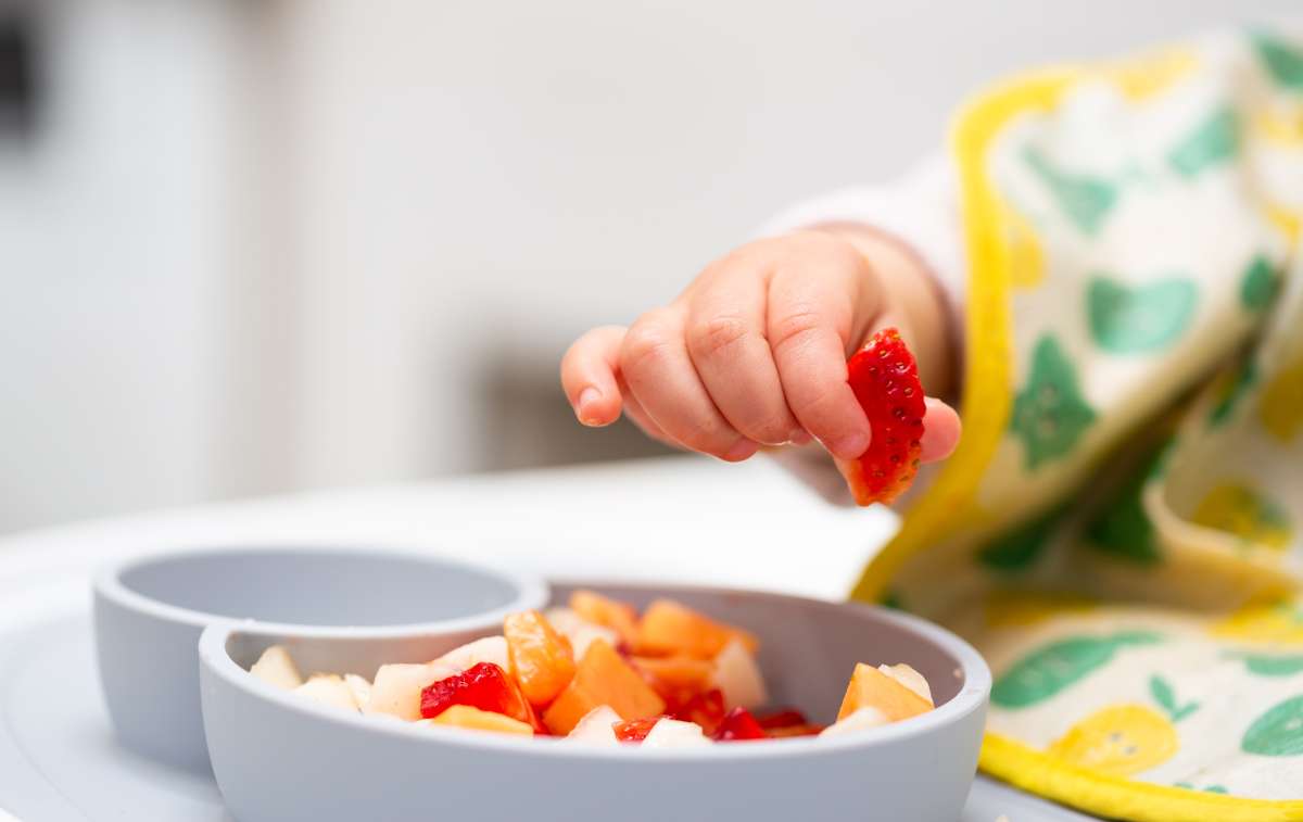 Baby Hand with a Piece of Fruits Sitting in Child's Chair Kid Eating Healthy Food-Salt Intake In Babies