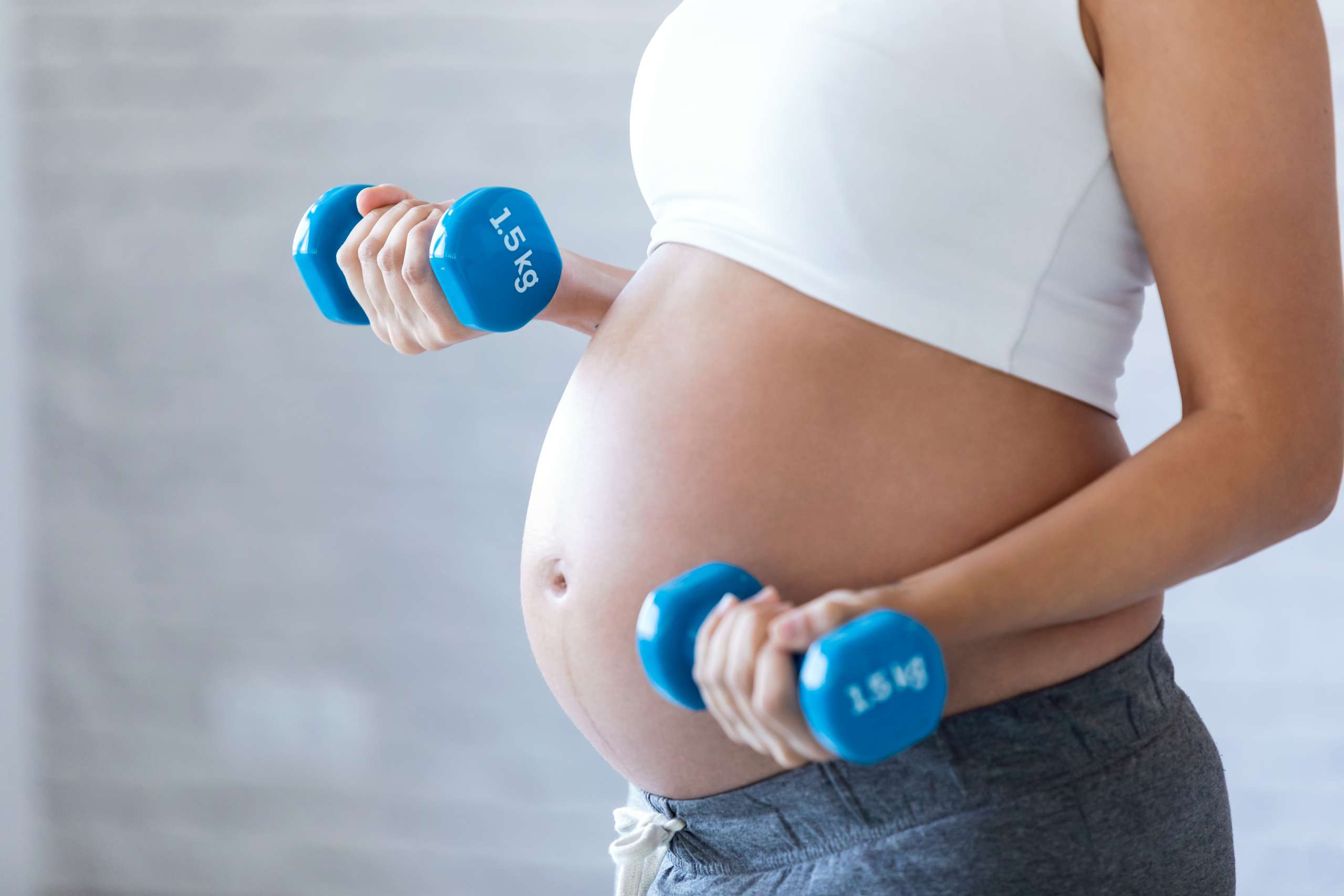 Pregnant woman doing exercise with dumbbells at home.