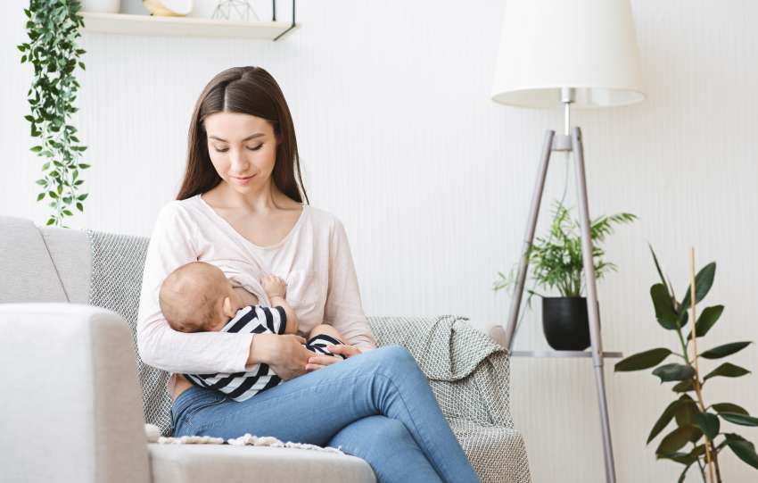 Beautiful young mother breastfeeding her baby on couch at home